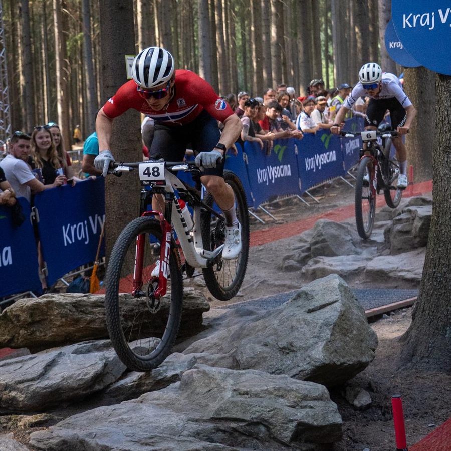 Norwegian rider in a red, white and blue jersey racing over rocks, spectators and barriers along the course